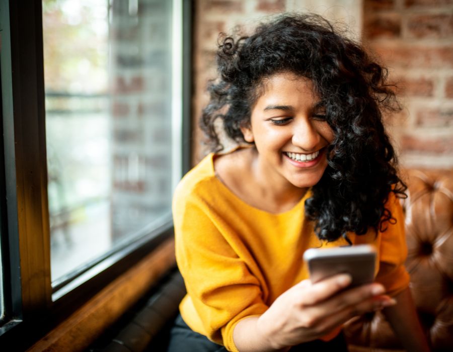 Girl in yellow sweater smiling at her cell phone