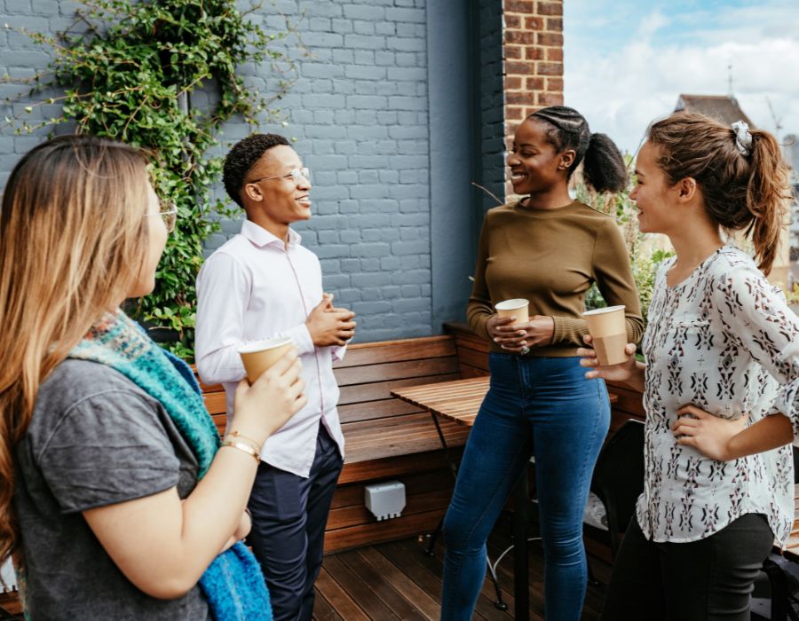 Group of young adults chatting in outdoor space with coffees